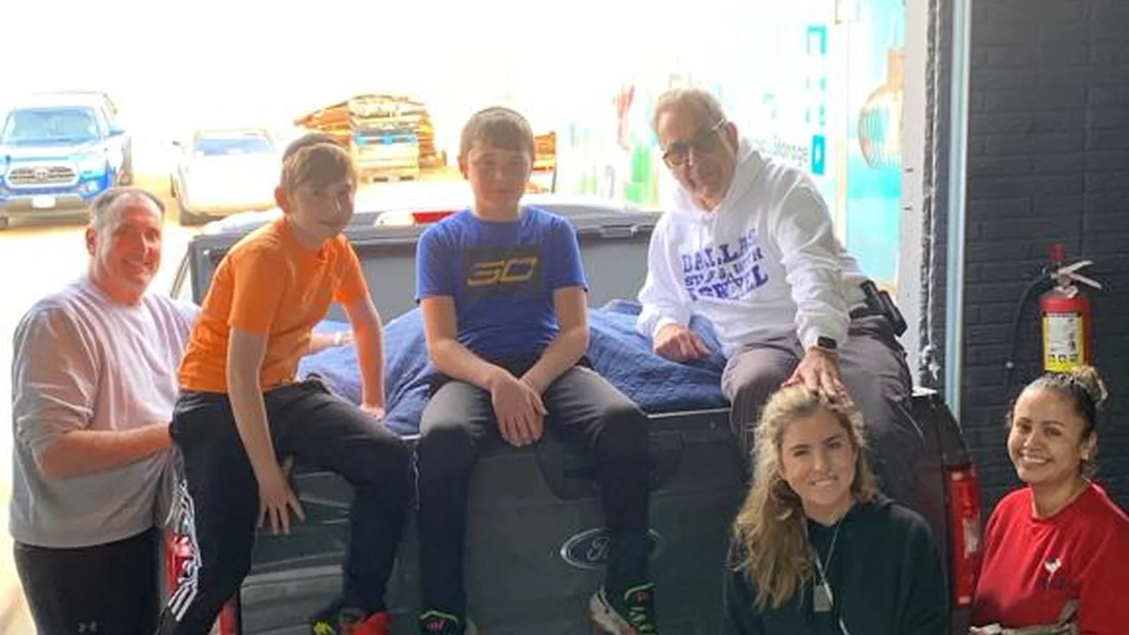 Volunteers of all ages, including several children, sitting in the back of a pickup truck at a Dallas packing day