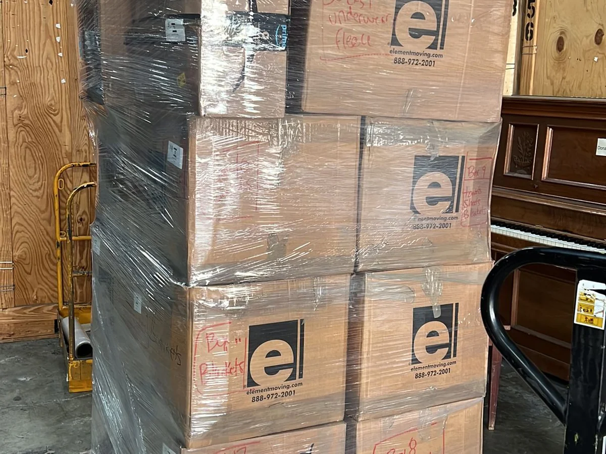 A shrink-wrapped pallet of donated supply boxes on a pallet jack, marked with the Element Moving logo