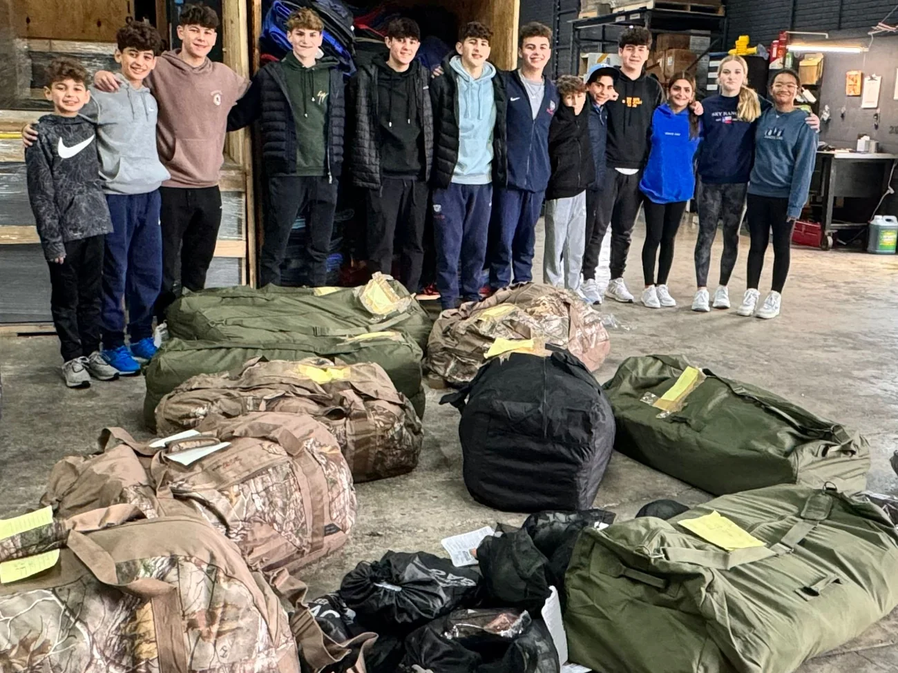 About a dozen teenage volunteers standing behind a row of packed duffel bags in a Dallas garage