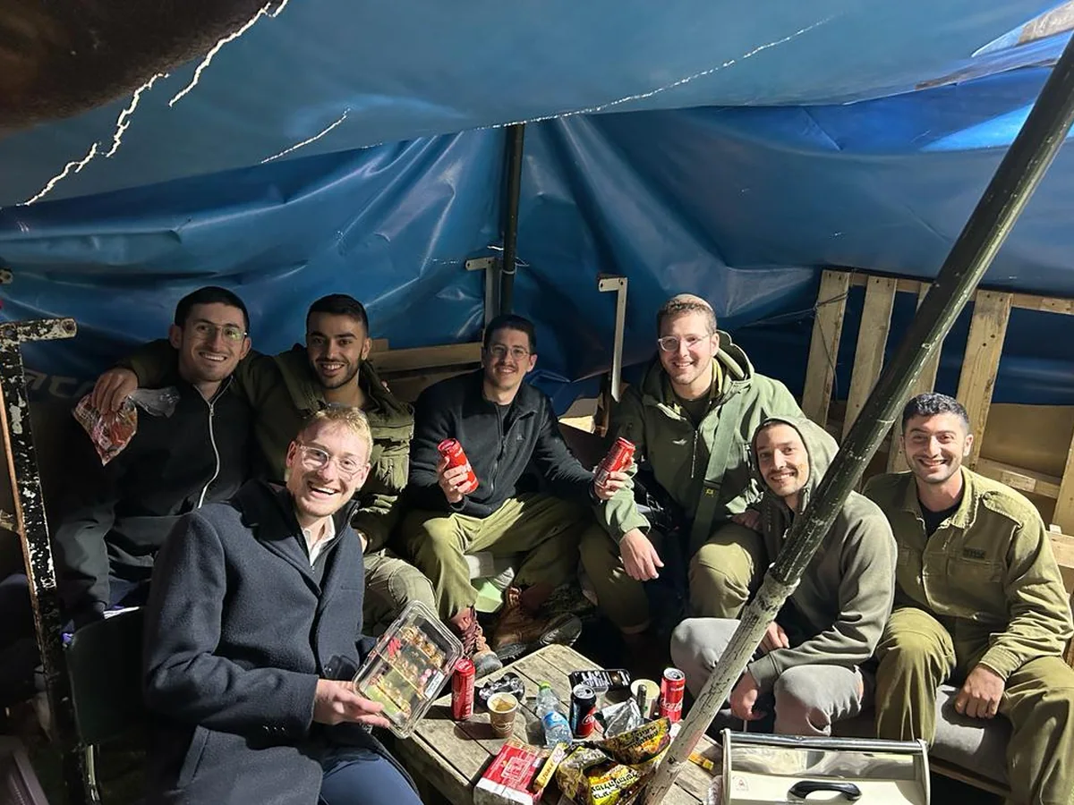 Israeli soldiers gathered under a tarpaulin at their post, holding drinks and supplies just delivered to them