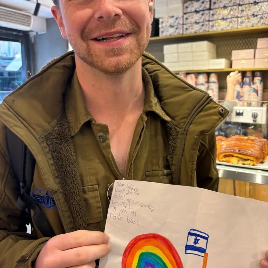 A smiling Israeli soldier holding up a child’s letter decorated with a rainbow and an Israeli flag