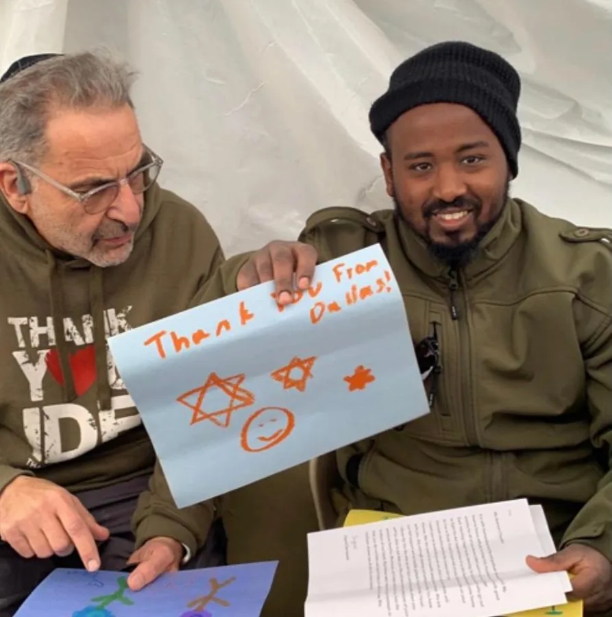 Ivan Sacks beside a soldier holding a hand-drawn sign reading “Thank you From Dallas” with Stars of David