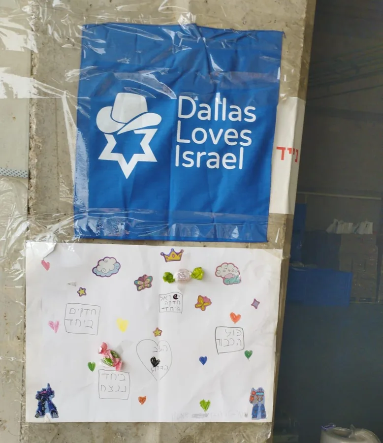 A “Dallas Loves Israel” banner pinned to a base wall above a children’s decorated poster