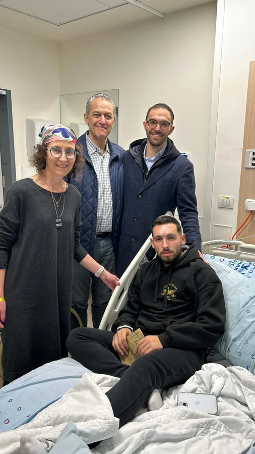 A family group standing at the hospital bedside of a recovering soldier
