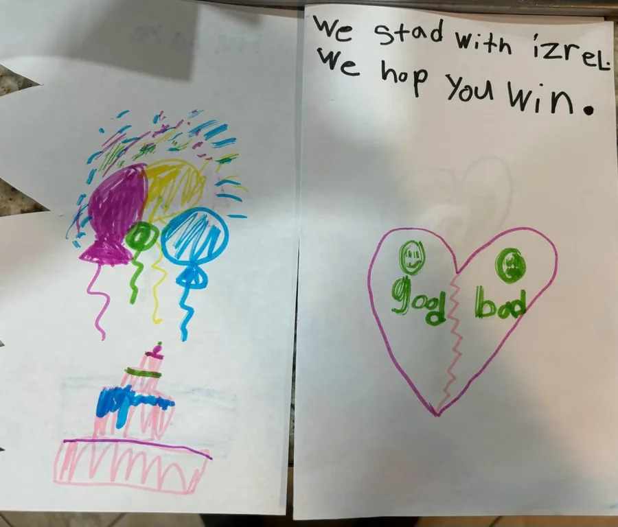 Two children’s letters opened side by side, one reading “We stand with Israel, we hope you win”