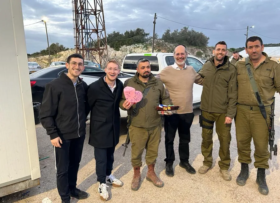 Volunteers and Israeli soldiers standing together outdoors, one holding a heart-shaped gift box